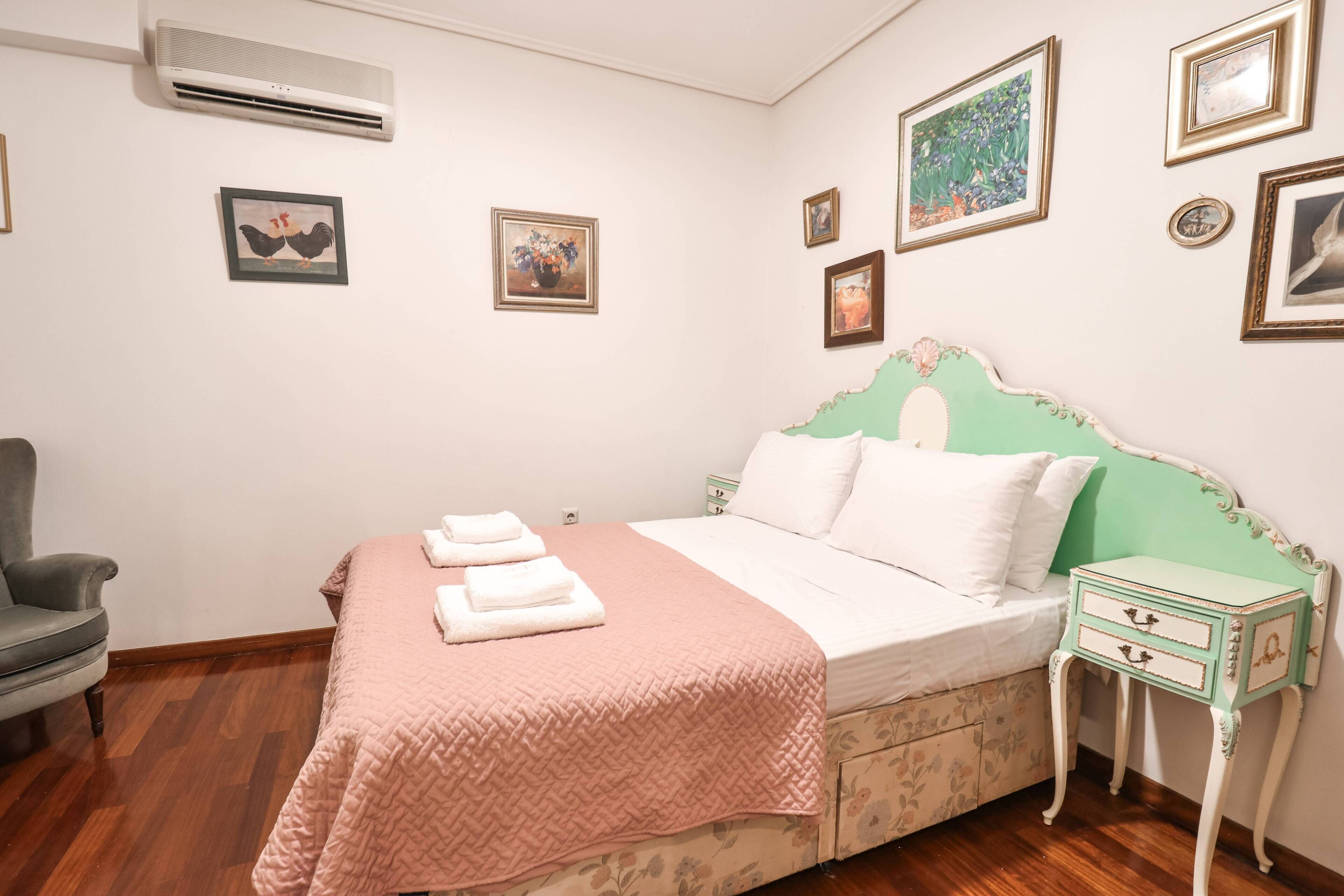 A bedroom with a bed, a chair, a nightstand, and wall-mounted pictures.