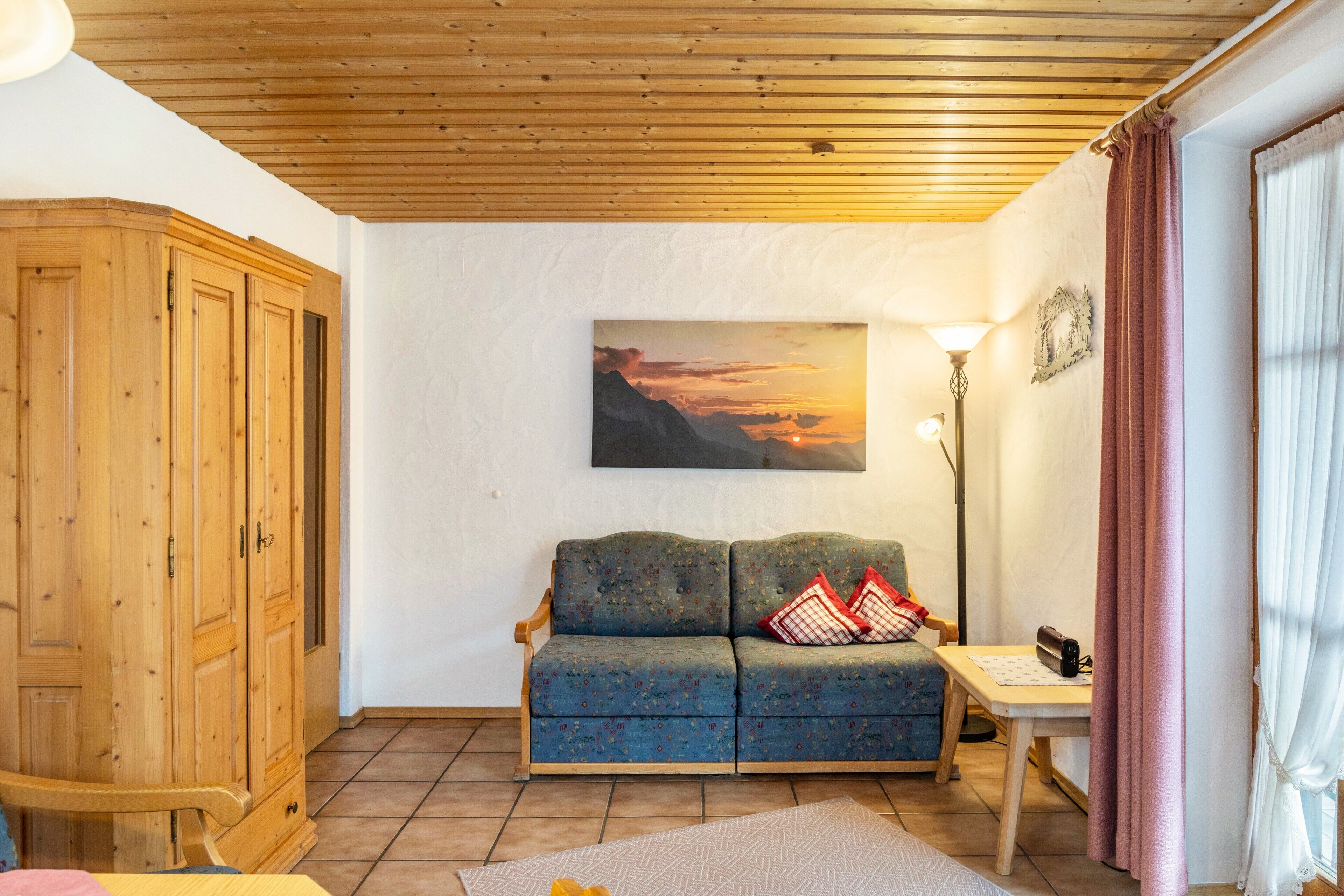 Una habitación con techo de madera, un sofá con cojines, una mesa con lámpara y un cuadro en la pared.