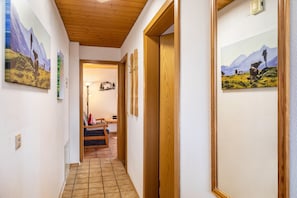 Un pasillo con puertas de madera, un banco y cuadros en las paredes.