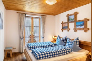 Una habitación con techo de madera, una cama con ropa de cama a cuadros, una mesita de noche con lámpara y una ventana con cortinas.