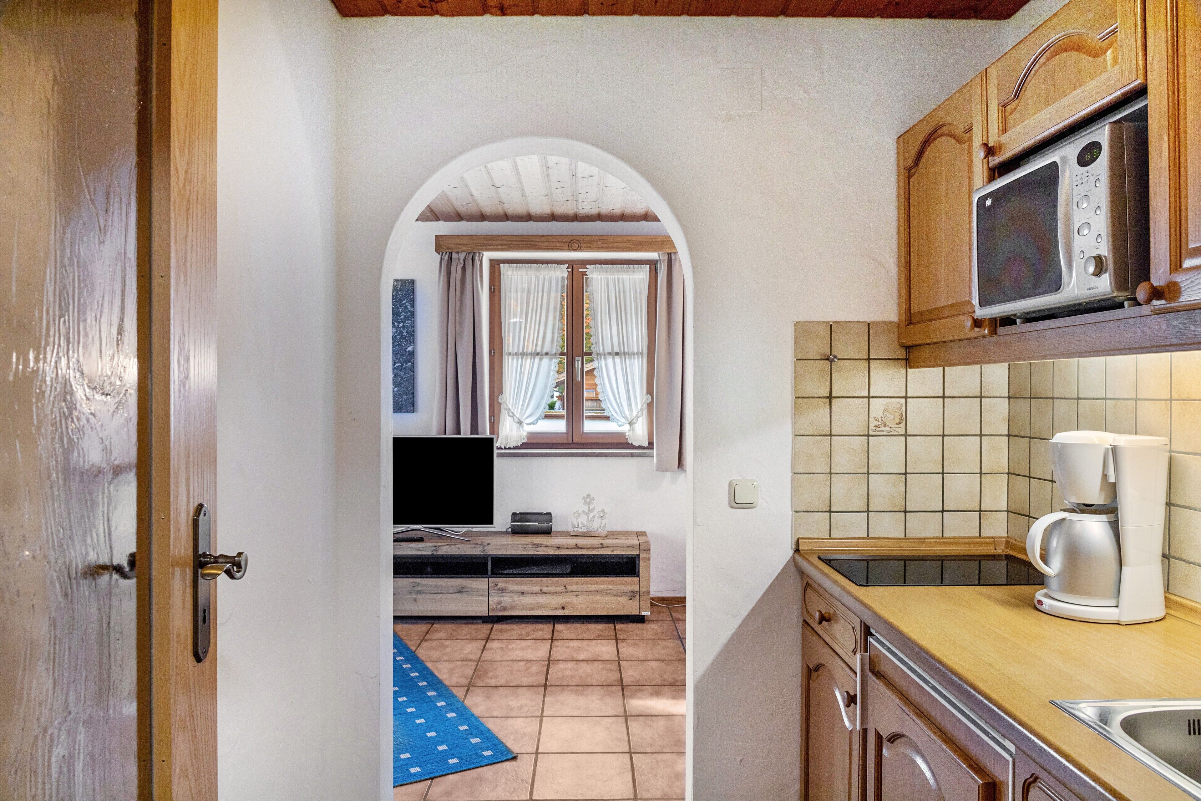 Una cocina compacta con microondas, cafetera y ventana con cortinas.