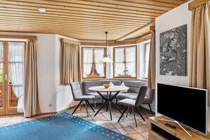 Una habitación con techo de madera, una mesa redonda con sillas, un sofá, un televisor y un cuadro en la pared.