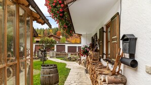 A stone pathway leading to a white building with wooden shutters, a wooden barrel, and a rustic outdoor setting. - Studio 'Burgberg' with Mountain View, Balcony and Wi-Fi (Mittenwald)