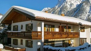 A two-story chalet with a balcony, set against a snowy mountain backdrop. - Studio 'Burgberg' with Mountain View, Balcony and Wi-Fi (Mittenwald)