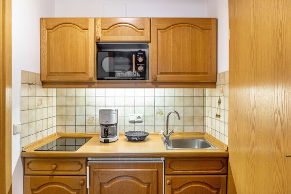 A kitchen with wooden cabinets, a microwave, a coffee maker, and a sink.