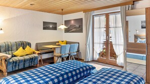 A cozy room with a sofa, a dining table with chairs, a bed with a checkered bedspread, and a wooden ceiling. - Studio 'Burgberg' with Mountain View, Balcony and Wi-Fi (Mittenwald)