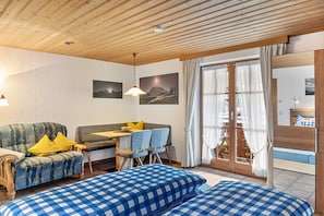 A cozy room with a sofa, a dining table with chairs, a bed with a checkered bedspread, and a wooden ceiling. - Studio 'Burgberg' with Mountain View, Balcony and Wi-Fi (Mittenwald)