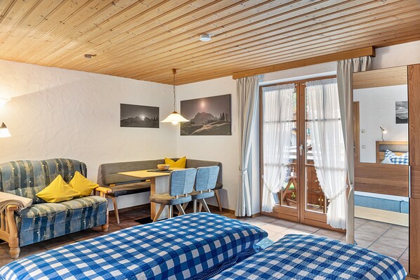 A cozy room with a sofa, a dining table with chairs, a bed with a checkered bedspread, and a wooden ceiling. - Studio 'Burgberg' with Mountain View, Balcony and Wi-Fi (Mittenwald)