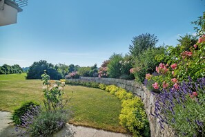 Een aangelegde tuin met een stenen muur, diverse bloeiende planten en een gazon.
