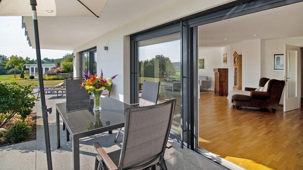 Een moderne kamer met een glazen deur naar een terras, een eettafel met stoelen en een groot raam.