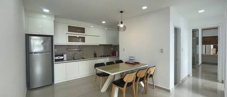 Una cocina moderna con refrigerador empotrado, una mesa de comedor con sillas y una lámpara colgante.