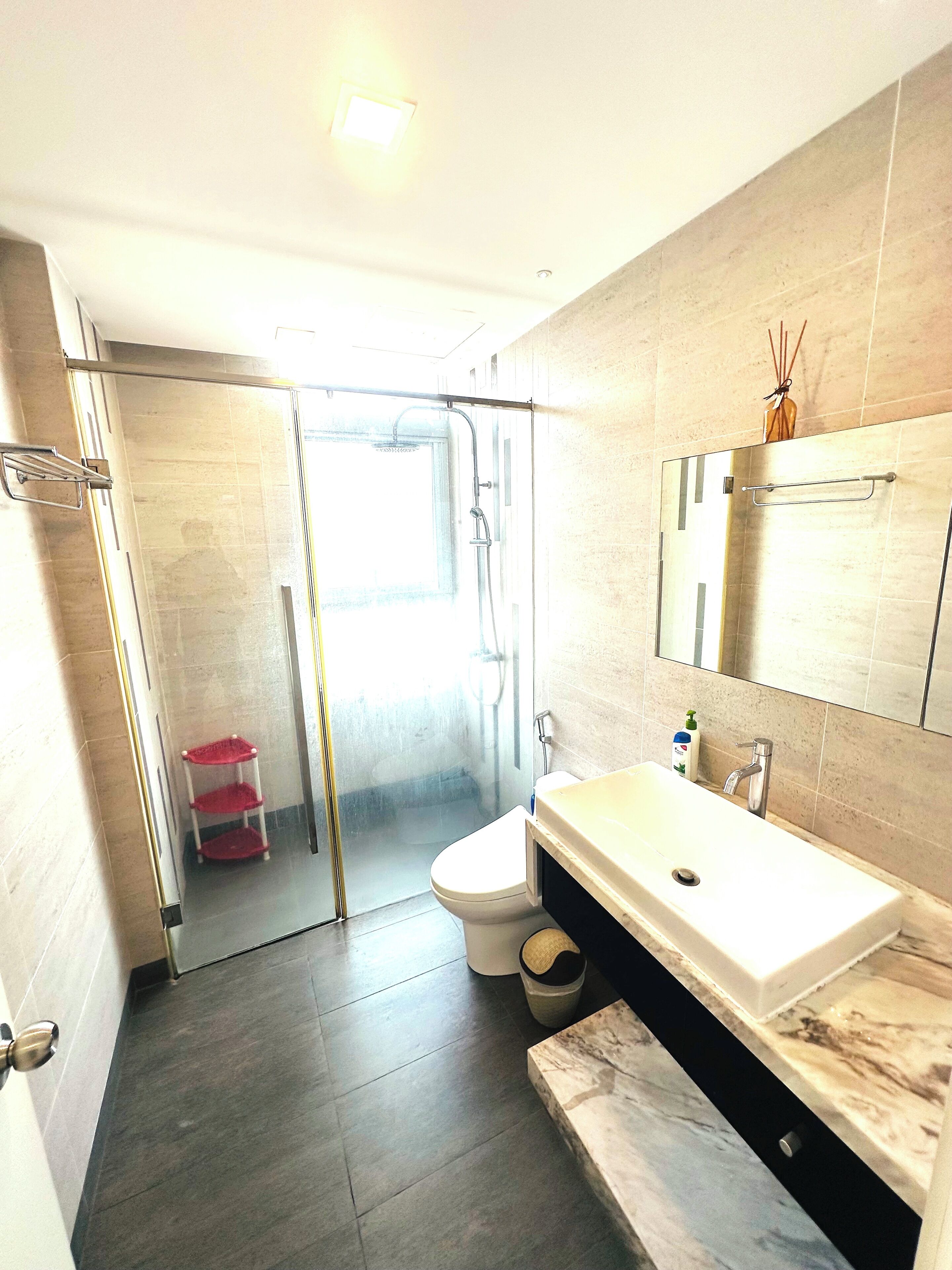 A modern bathroom with a glass shower enclosure, a white sink with a marble countertop, and a toilet.