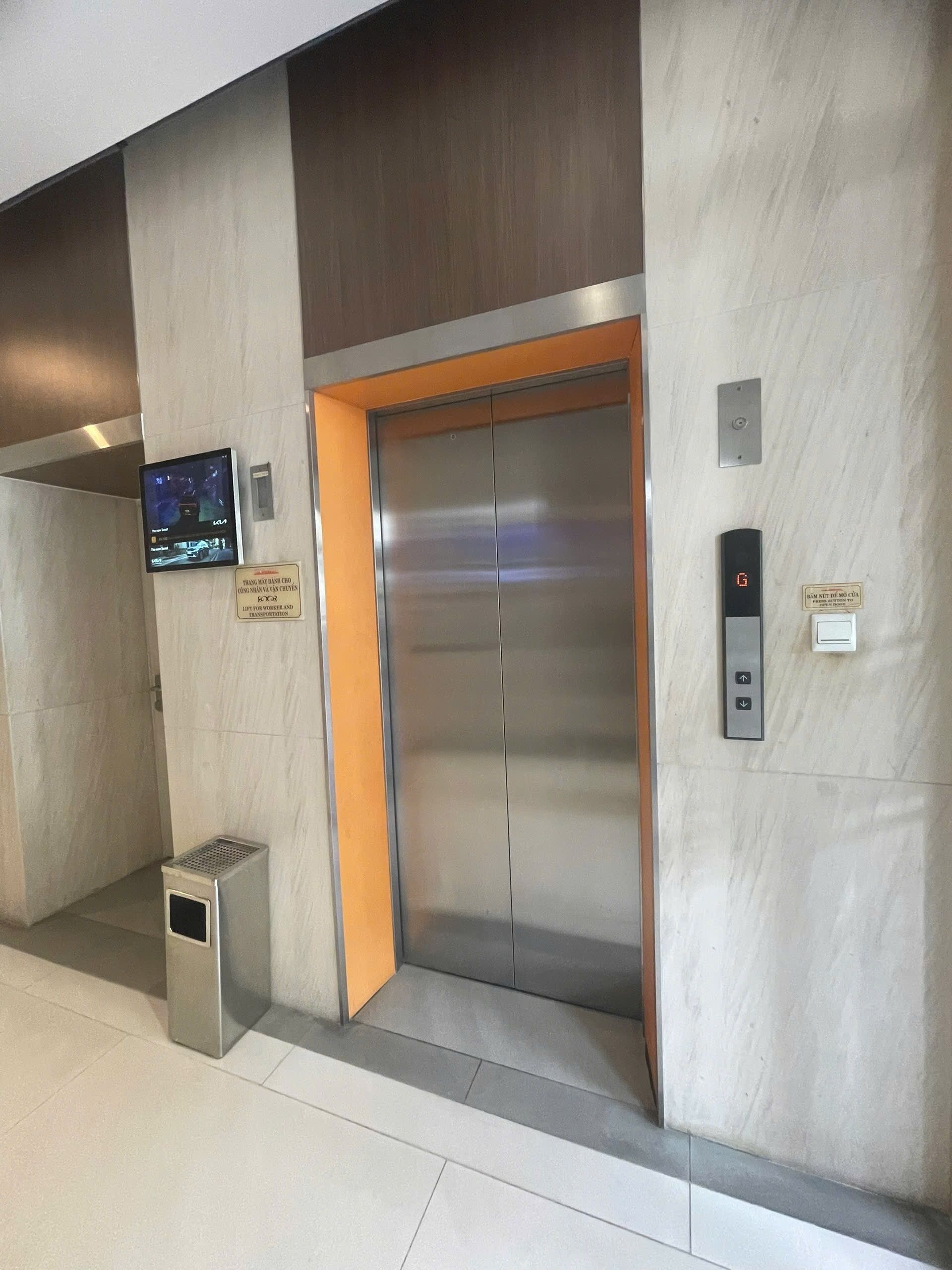 An elevator with a digital display, a trash bin, and a sign indicating it is for workers and transportation.