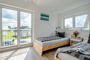 Une chambre à coucher avec un lit, un bureau, une fenêtre donnant sur des maisons et un tableau accroché au mur.