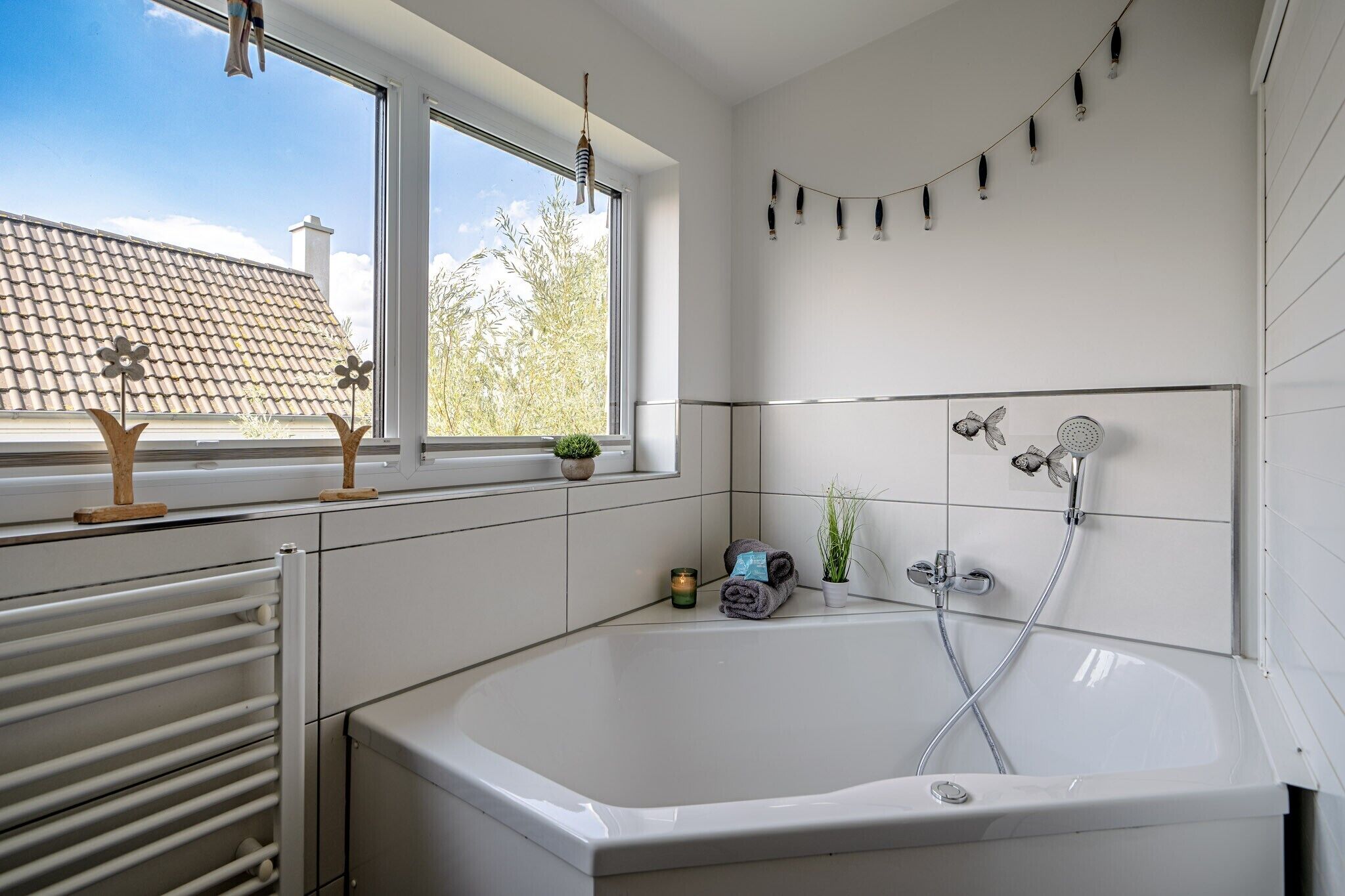 A modern bathroom with a large bathtub, a window with a view of a tiled roof, and a wall-mounted shower.