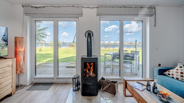 Una sala de estar moderna con estufa de leña, ventanas amplias, un sofá y un comedor.