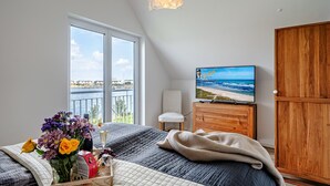 Un dormitorio con una ventana grande, una cama, un televisor, un armario de madera y un balcón con vista al mar.