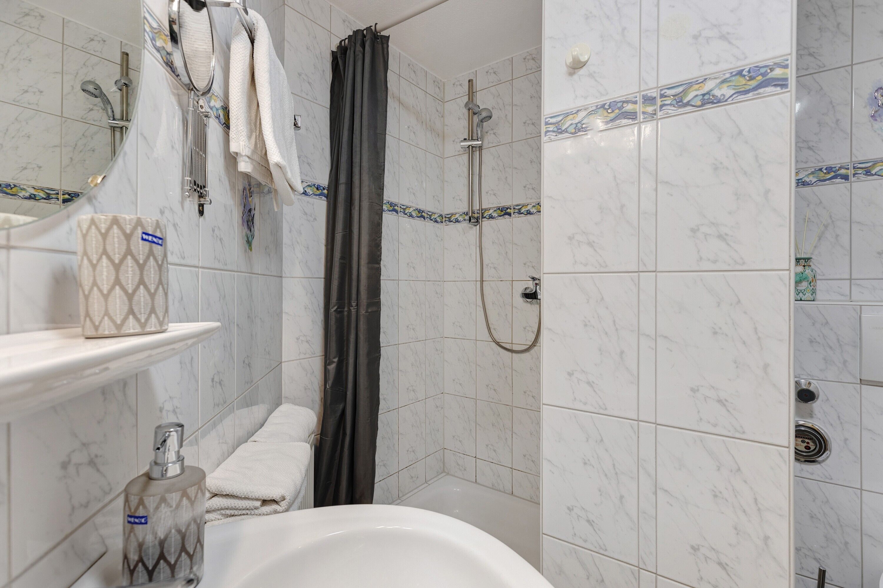 Een badkamer met een witte badkuip, een douche met gordijn, een handdoekhouder en een zeepdispenser.