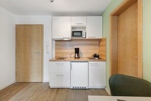 A compact kitchen with white cabinets, a microwave, a coffee maker, and a sink.