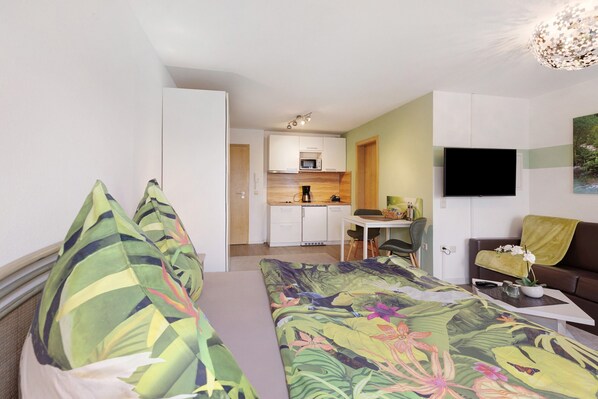 A bedroom with a bed, pillows, a desk, a chair, a television, and a sofa.