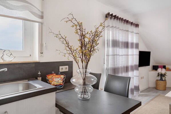 A modern kitchen with a double sink, a vase with branches, and a dining area with a table and chairs.