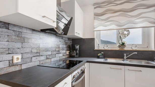 A modern kitchen with a stone backsplash, a built-in oven, and a window with a view.