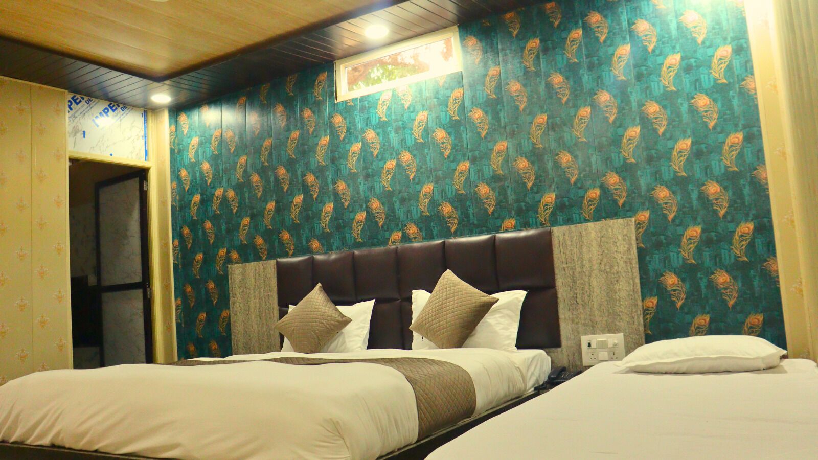 A hotel room with two beds, a dark headboard, and patterned wallpaper.
