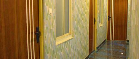 Un couloir avec des portes en bois, un mur orné de motifs et un sol en marbre.