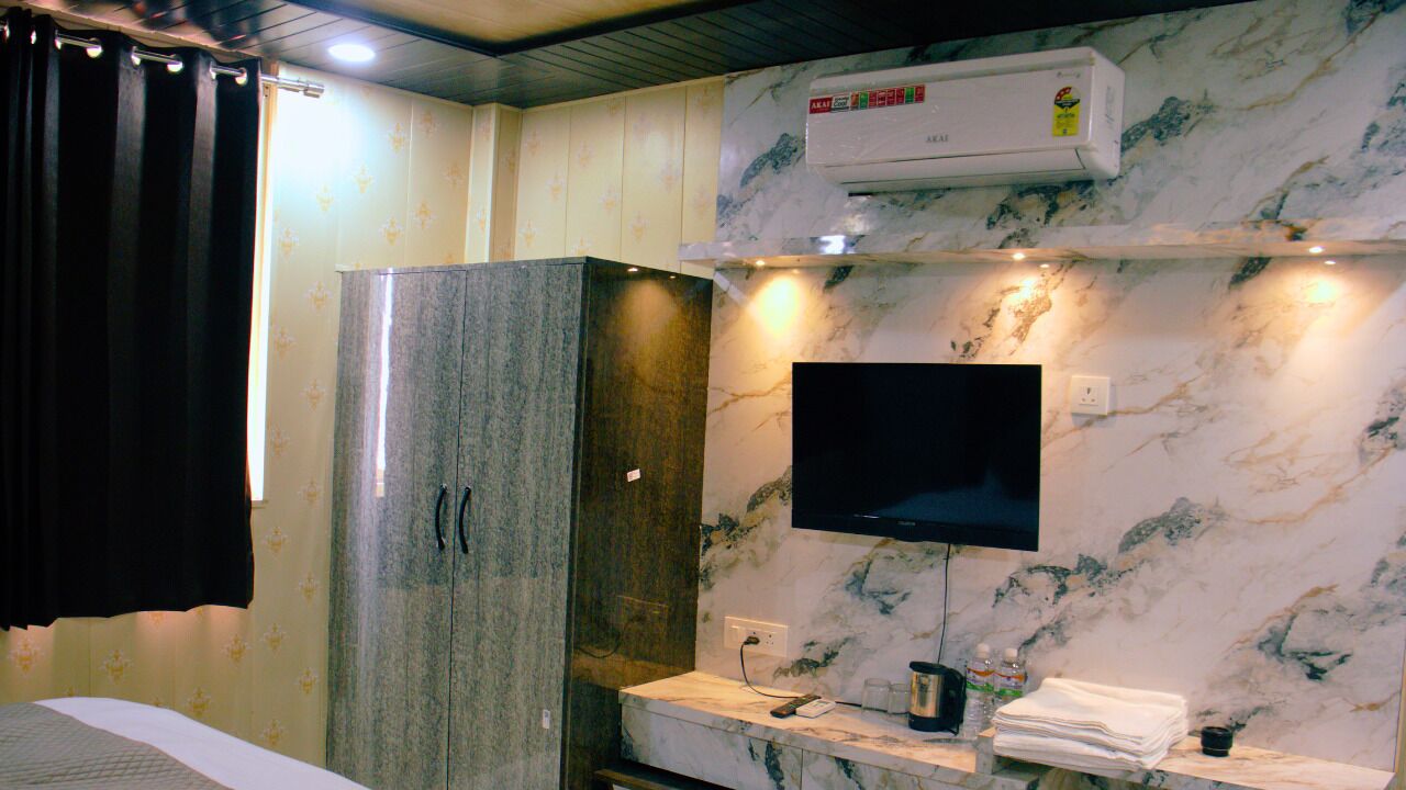 Habitación de hotel con pared de mármol, televisor de pantalla plana sobre una encimera de mármol, armario empotrado y unidad de aire acondicionado.