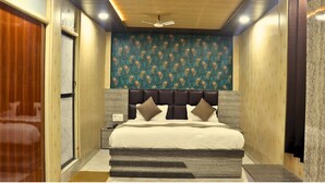 A bedroom with a bed, a headboard, a nightstand, and a wall with a patterned wallpaper. - GANGA RIVERFRONT ROOMS AND BANQUET (Prayagraj)