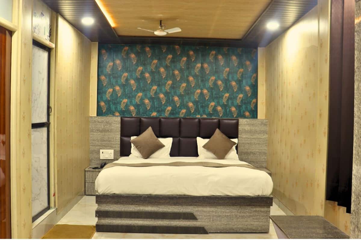 Quarto com cama, cabeceira, mesa de cabeceira e parede com papel de parede estampado.