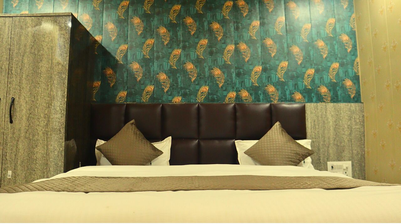 A hotel room with a large bed, a dark headboard, and patterned wallpaper.