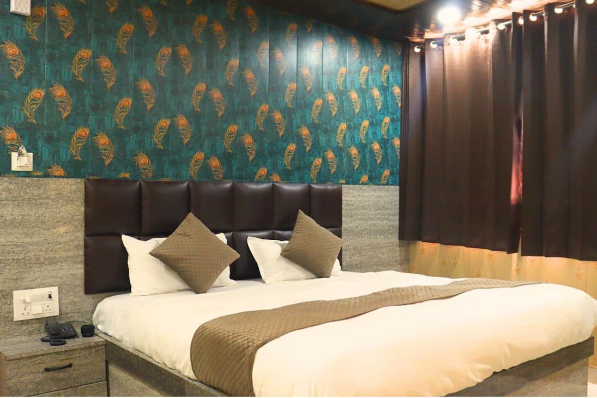 Quarto de hotel com uma cama grande, cabeceira, mesa de cabeceira com telefone e parede com padrão decorativo.