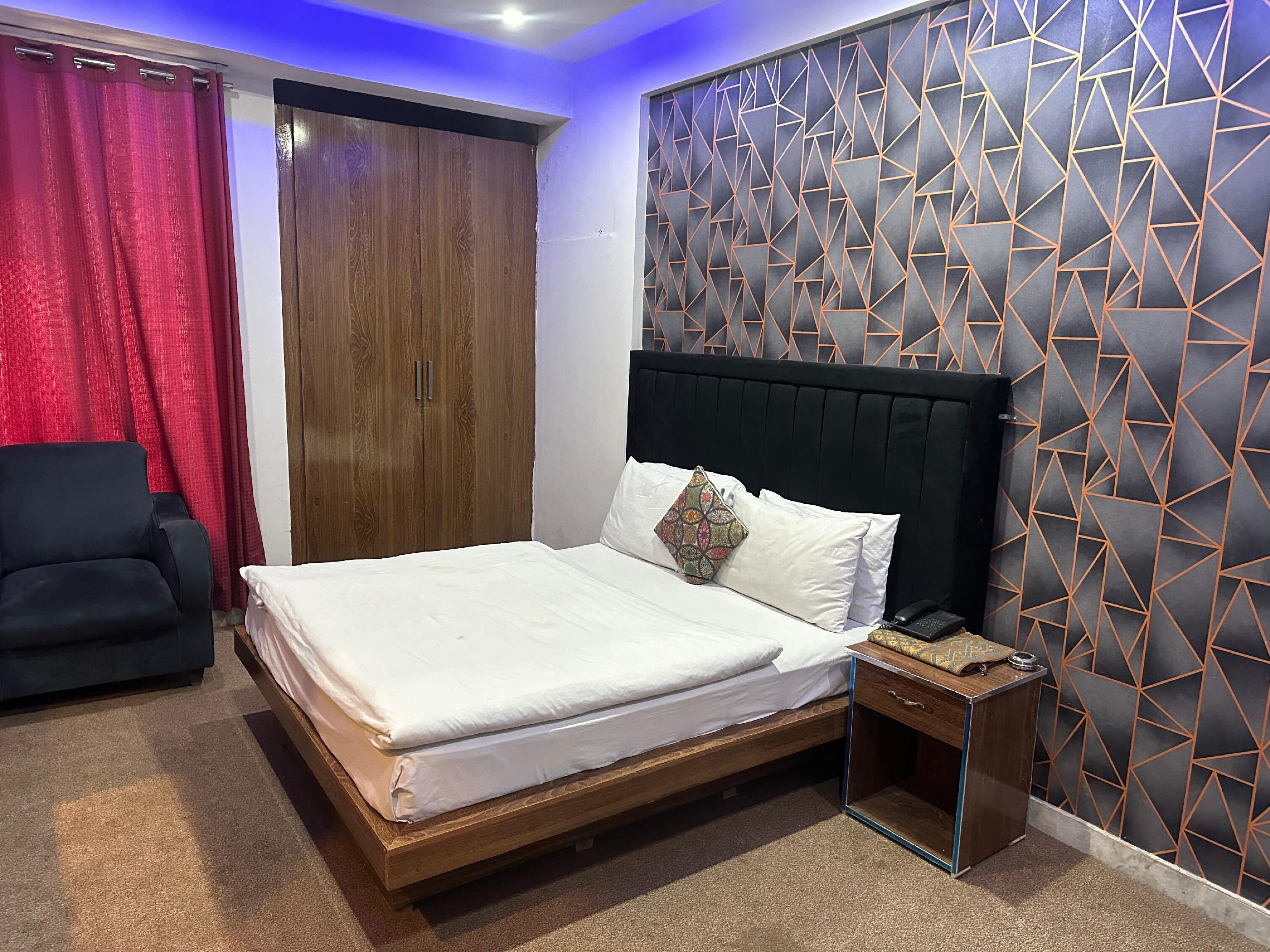 Un dormitorio con una cama de madera, una silla negra, un armario y una pared con un diseño geométrico.