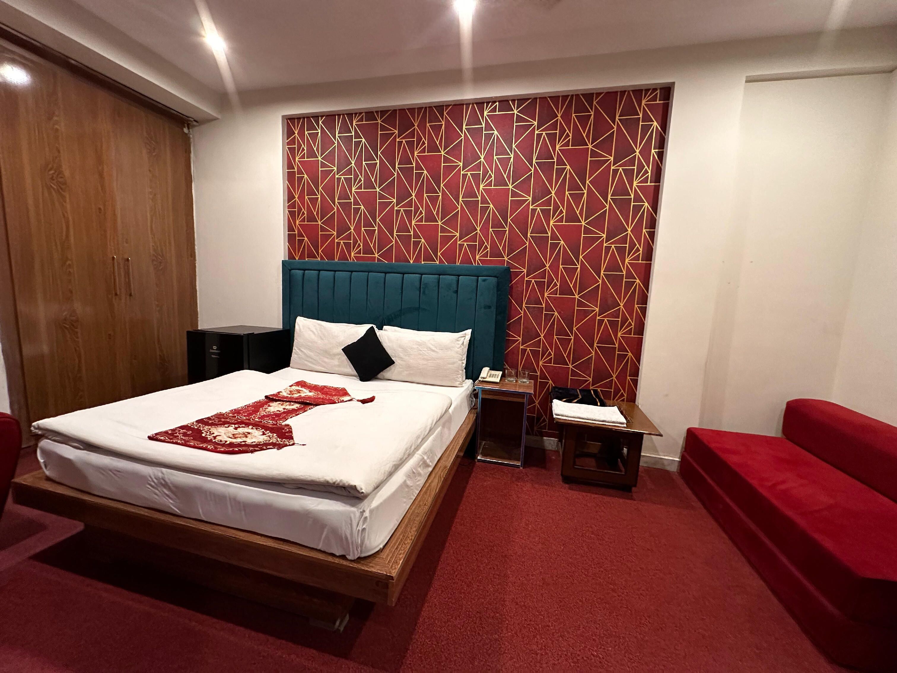 Een slaapkamer met een bed, een rood tapijt, een houten garderobe, een nachtkastje en een rode bank.