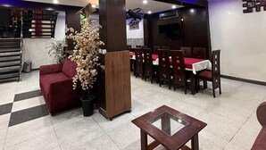 A hotel lobby with a checkered floor, a red sofa, a glass-top table, and a dining area with red tablecloths and wooden chairs. - Prime Inn Hotel (Rawalpindi)