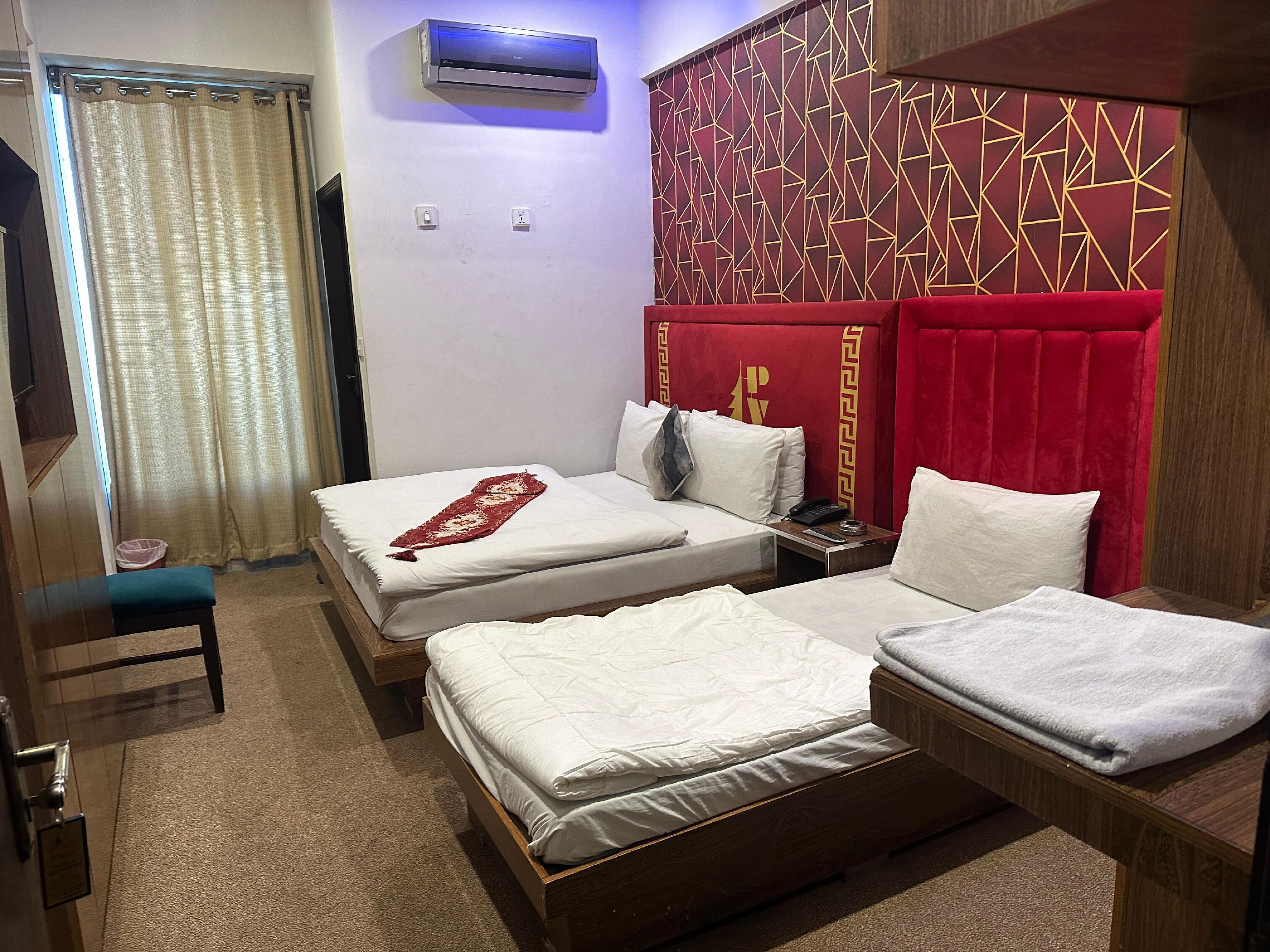Une chambre d’hôtel avec deux lits, une tête de lit rouge, un climatiseur et une petite table sur laquelle se trouvent un téléphone et une télécommande.