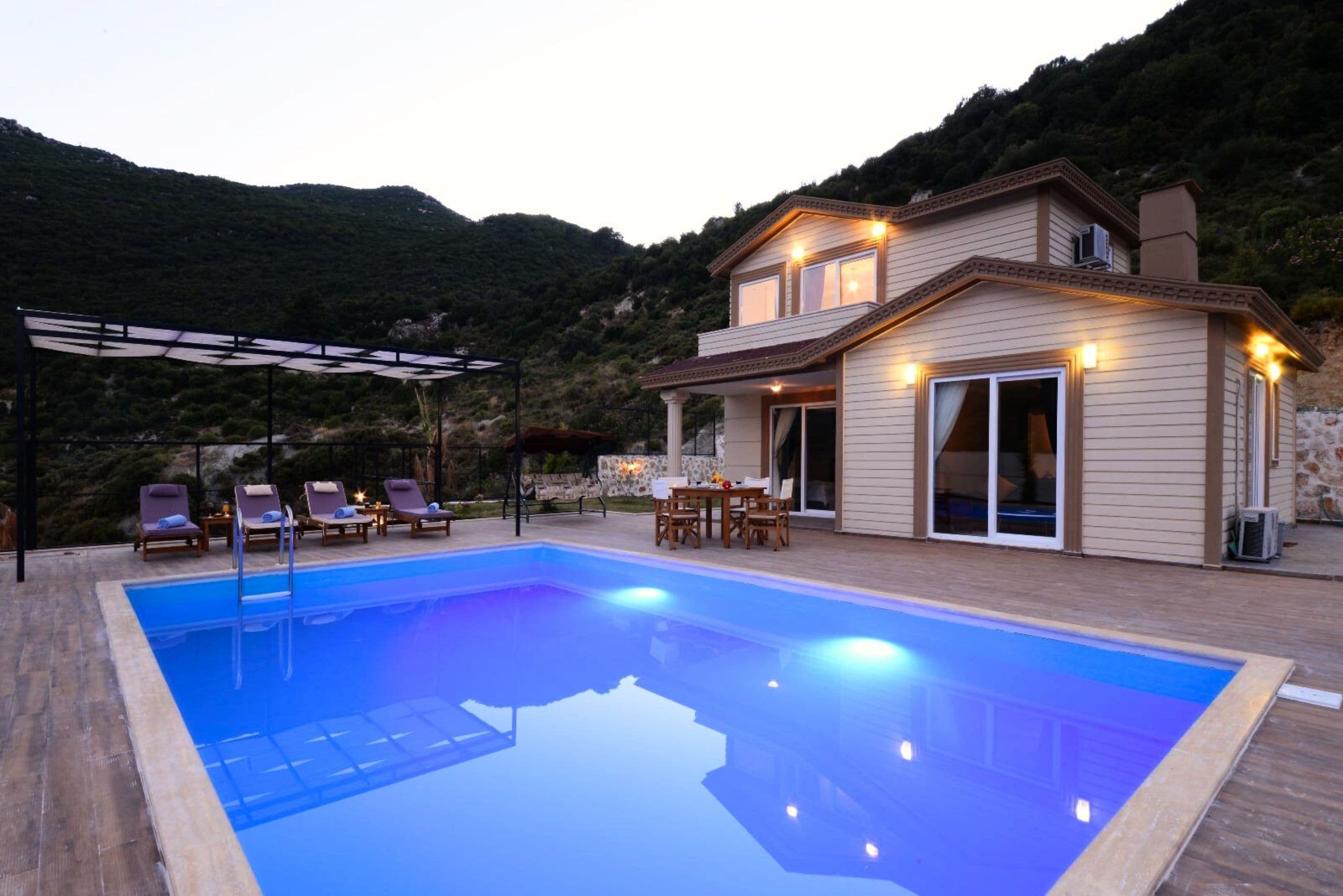 A two-story house with a swimming pool, outdoor seating, and a mountain backdrop.