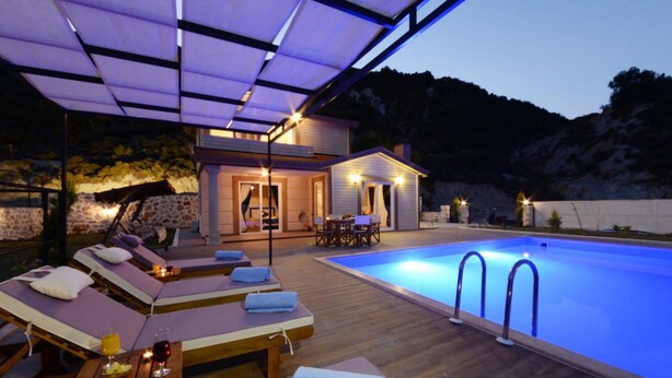 A poolside area with sun loungers, a small building with a pool, and a wooden deck. - Medis Vilları (Kaş)