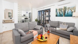 Una sala de estar moderna con dos sofás grises, una mesa de centro de madera con fruta, y una cocina al fondo.