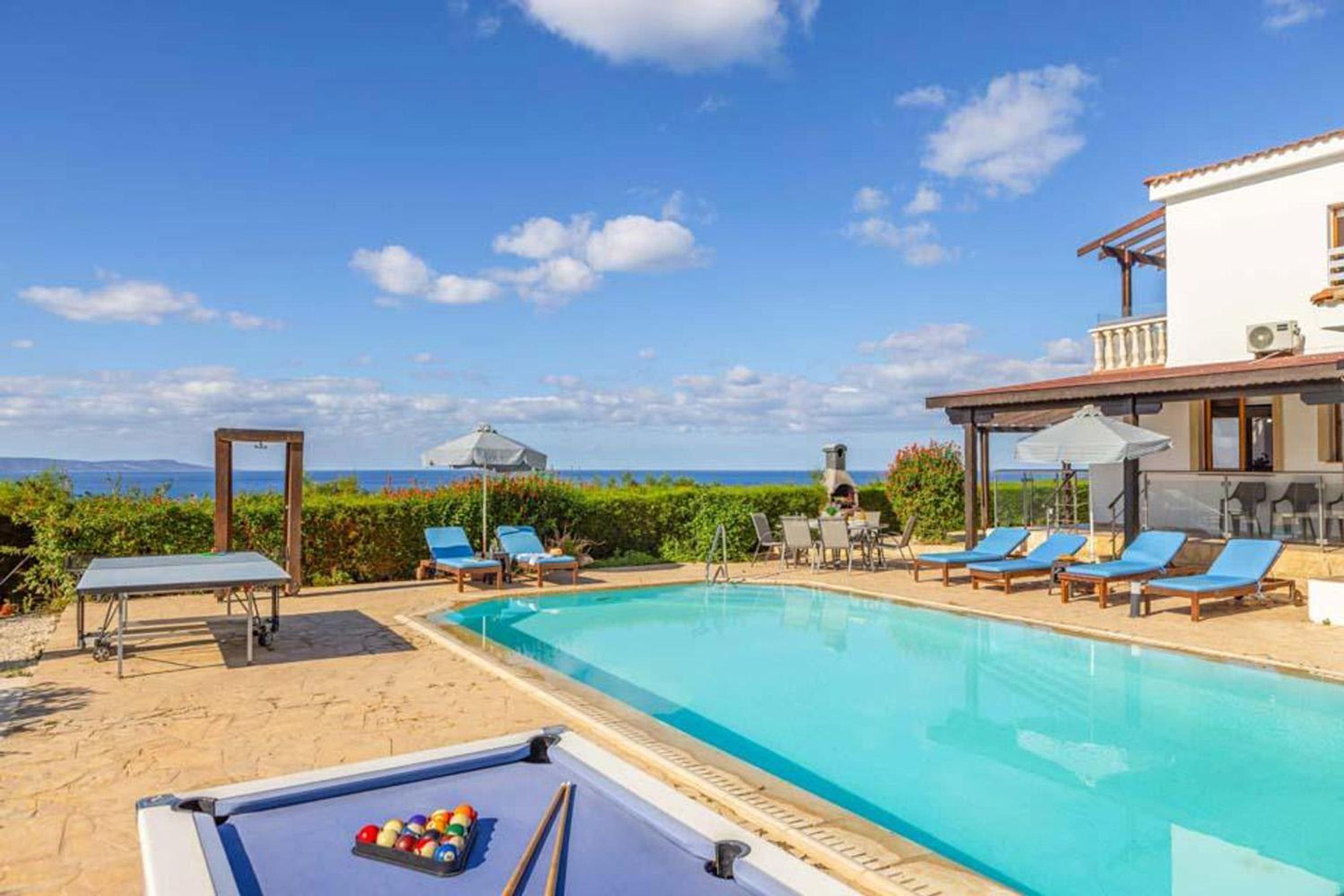 Zona de piscina con sillones, una mesa y vista al mar.