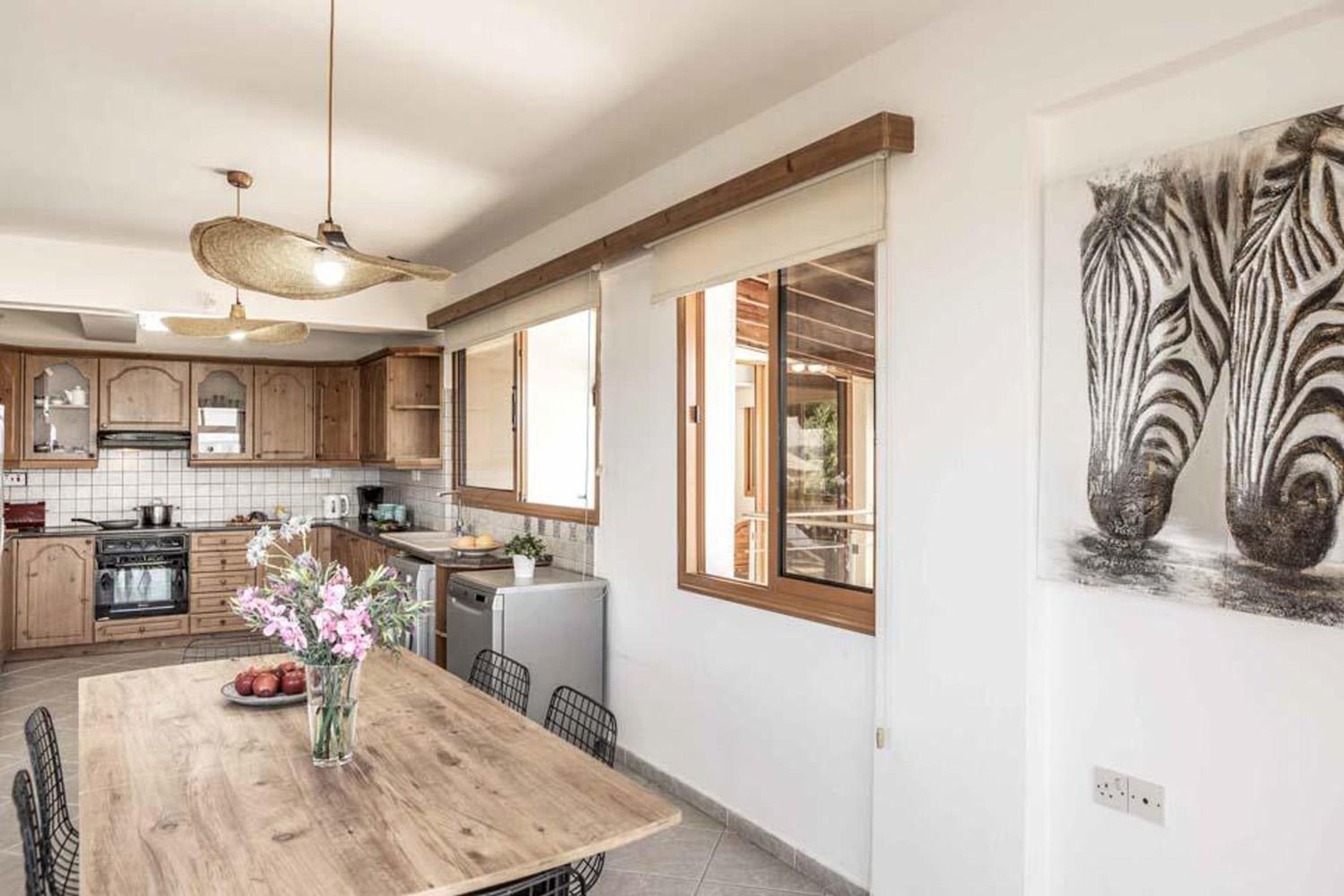 A kitchen with wooden cabinets, a dining table with chairs, and a large window.