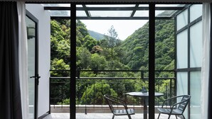 Ein Balkon mit Glastür, Tisch und zwei Stühlen mit Blick auf eine üppige grüne Landschaft.