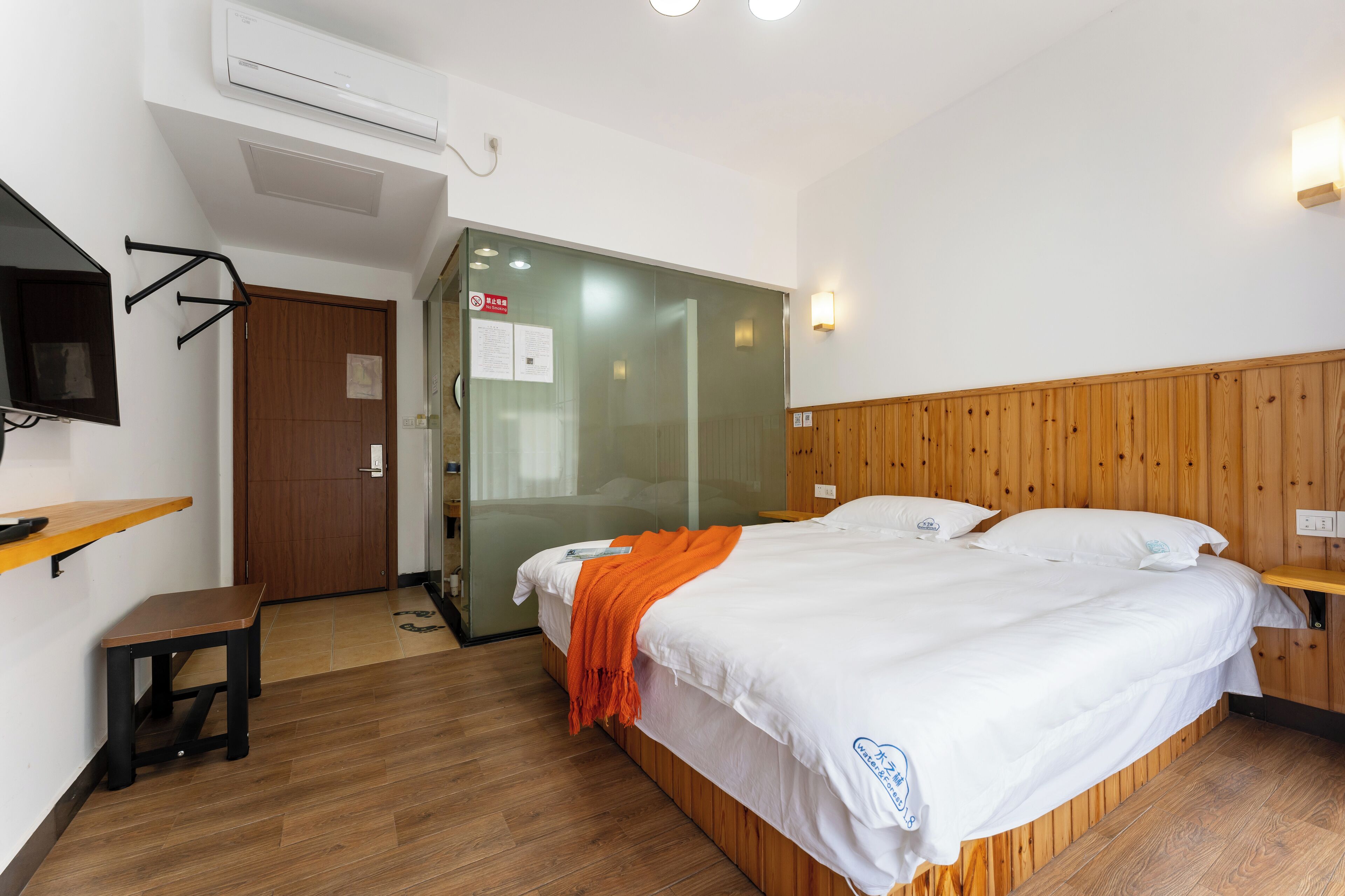 Una camera d'albergo con un letto di legno, una scrivania, una sedia, una televisione e un armadio.