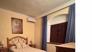 Een slaapkamer met een bed, nachtkastje, dressoir en raam met gordijnen.