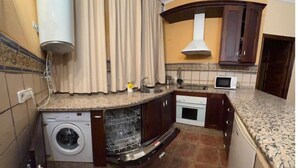 Een kleine keuken met een wasmachine, een magnetron en een fornuis.