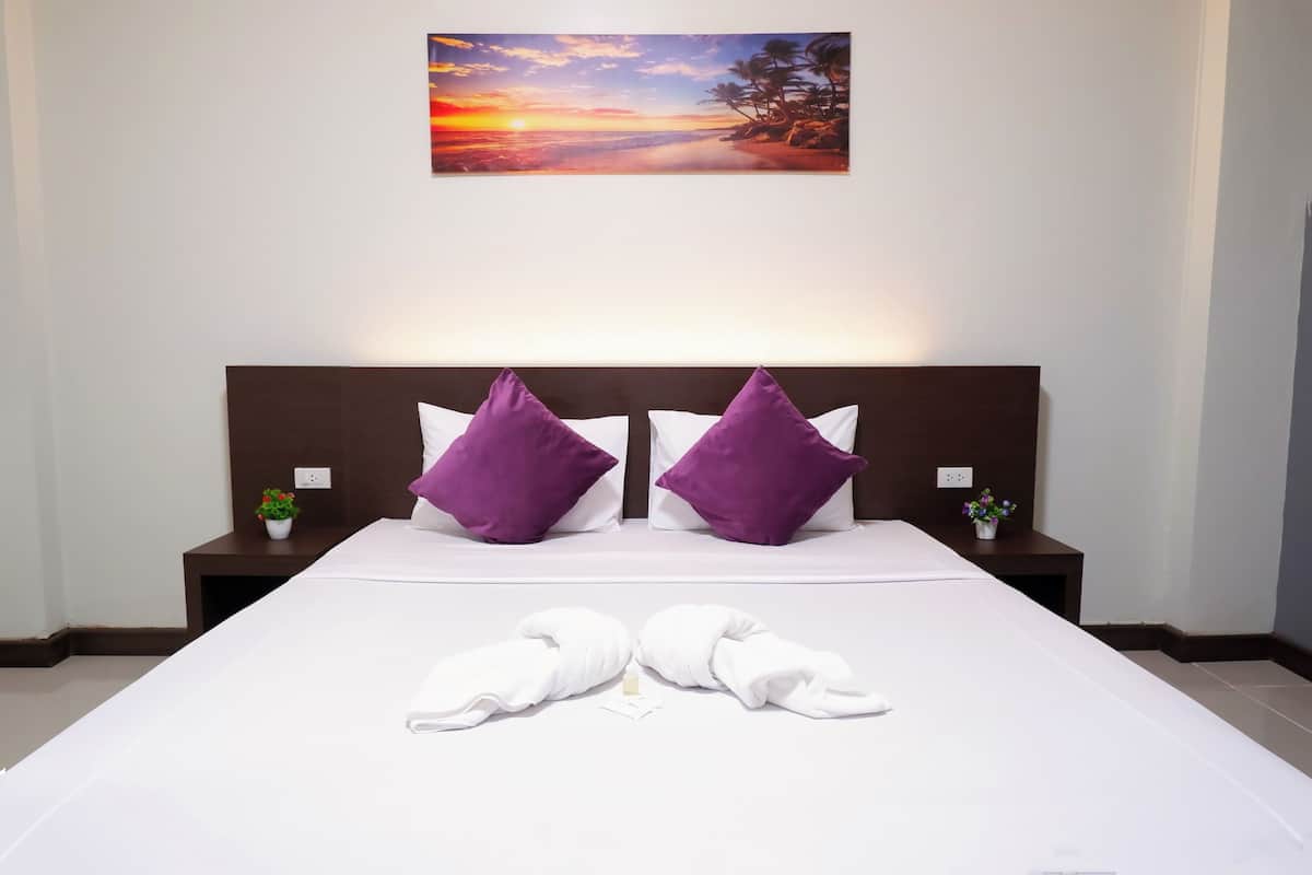 Una cama bien tendida con sábanas blancas, dos almohadas moradas y dos toallas blancas dobladas al pie de la cama.
