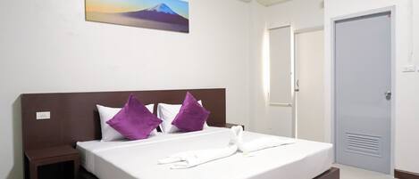 Habitación de hotel con cama, mesita de noche, un cuadro de una montaña y una puerta.