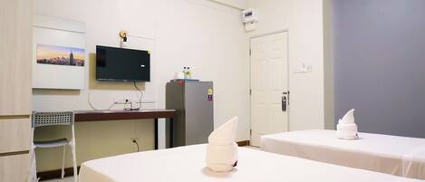 A hotel room with two beds, a desk with a chair, a television, a refrigerator, and a door.