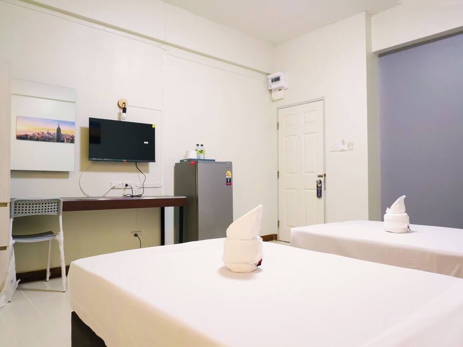 A hotel room with two beds, a desk with a chair, a television, a refrigerator, and a door.